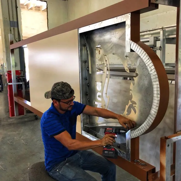 Fabricator forming a curved channel letter in the workshop